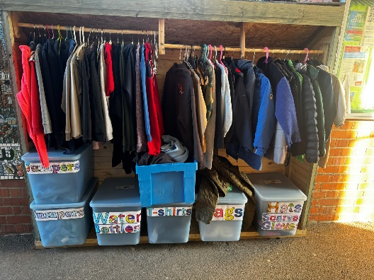 Built in cupboard with hanging rail with clothes hung and storage boxes