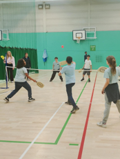 Children hitting a ball over a net in a gym similar to badminton but padel