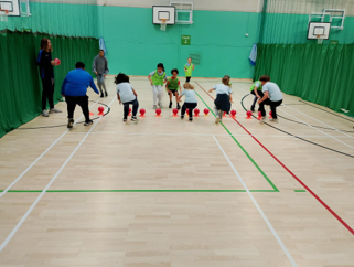 Children in a sports gym lined up in front of orange balls balancing on orange cones